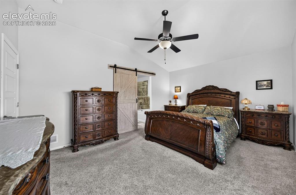 Image 19 of 40: MB featuring a vaulted ceiling with a ceiling fan, a white barn door, and a