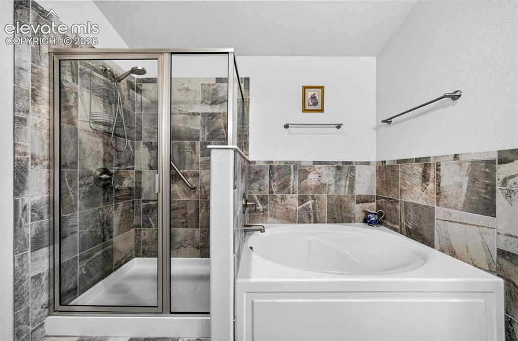 Image 25 of 40: Bathroom with a tiled shower enclosure featuring a glass door and an adjace