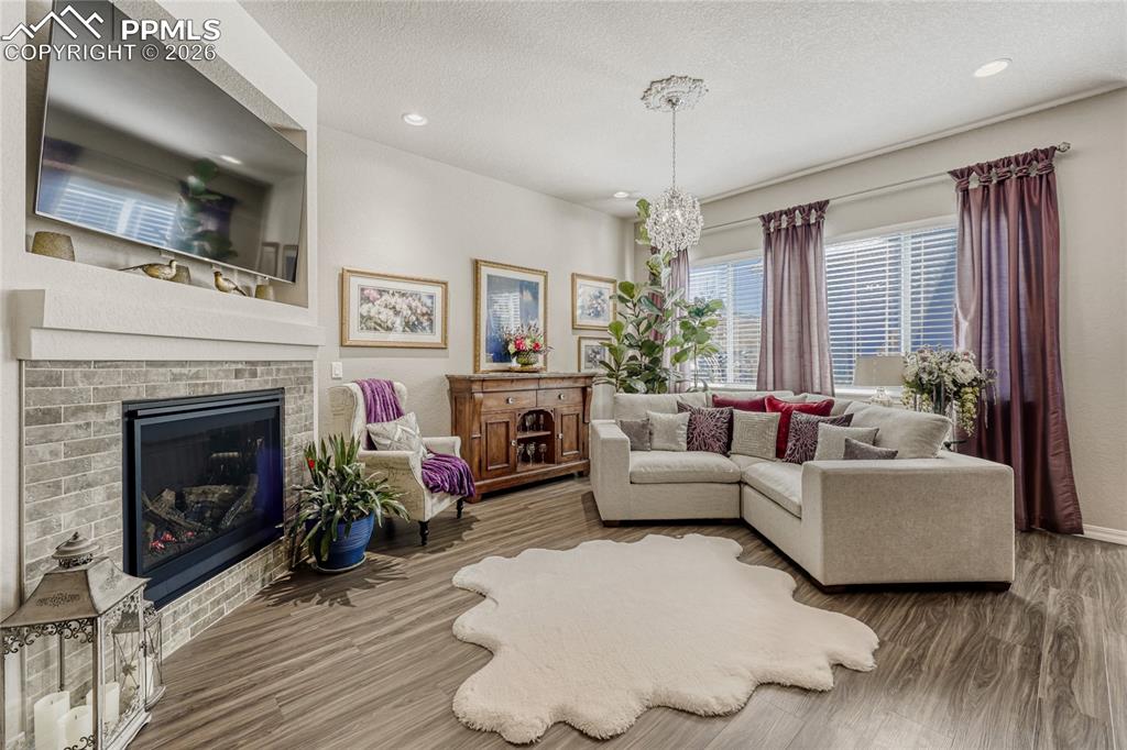 Image 13 of 30: Living room with a fireplace, LVP floors, and a chandelier