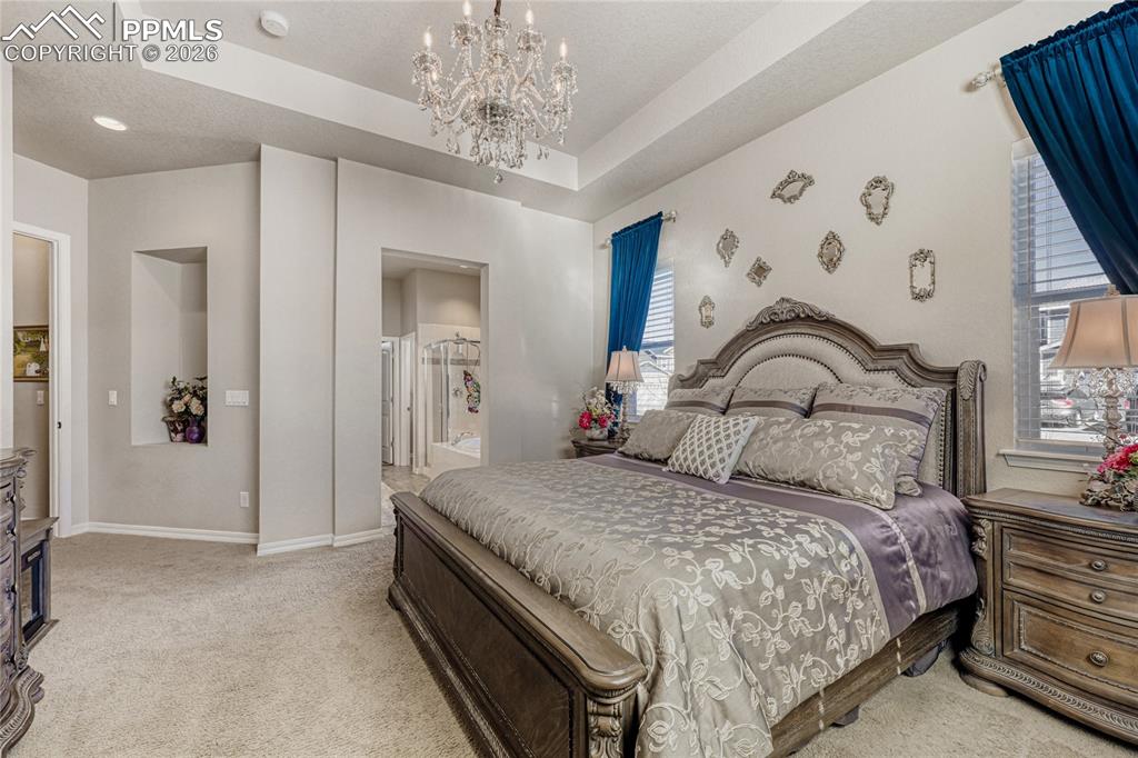 Image 18 of 30: Bedroom featuring a tray ceiling, ensuite bath, light carpet, and suspended