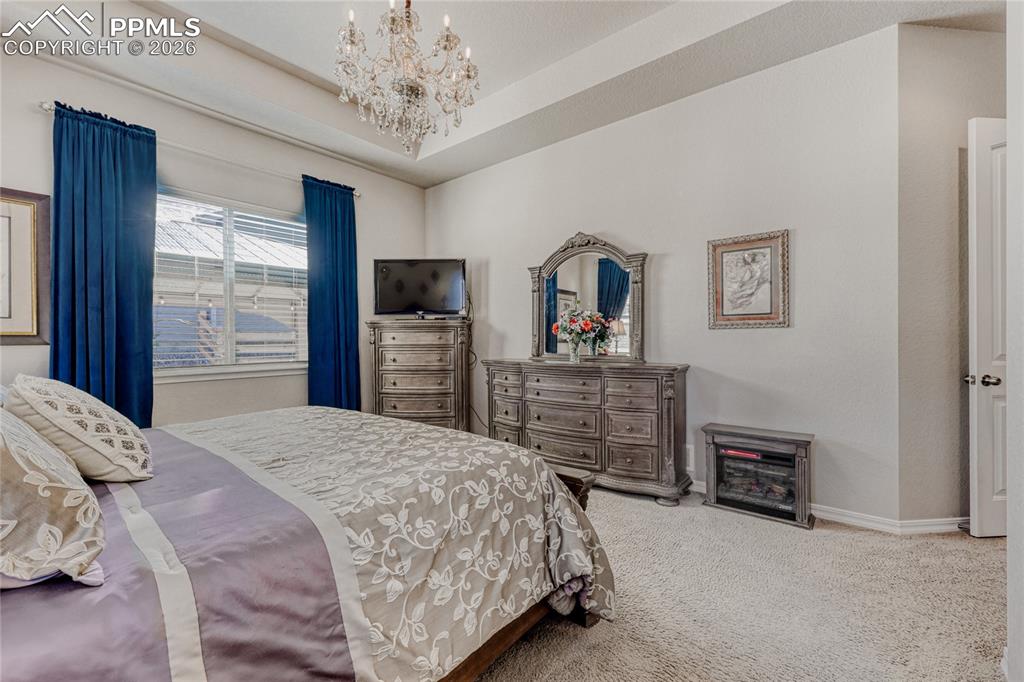 Image 19 of 30: Carpeted bedroom with a chandelier and a tray ceiling
