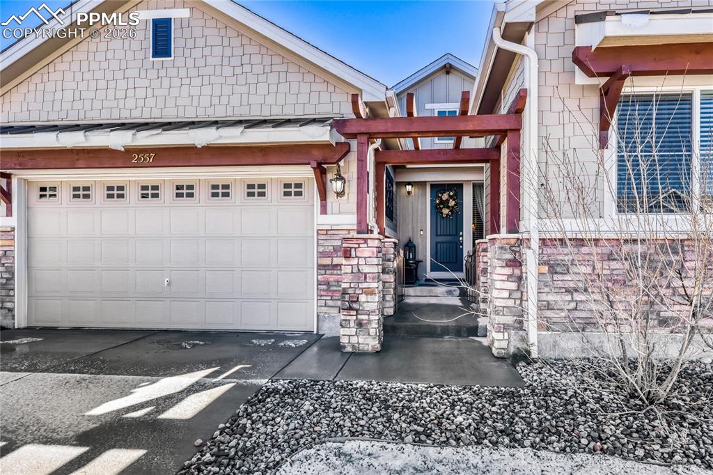 Image 3 of 30: View of front of property featuring stone siding, an attached garage, concr