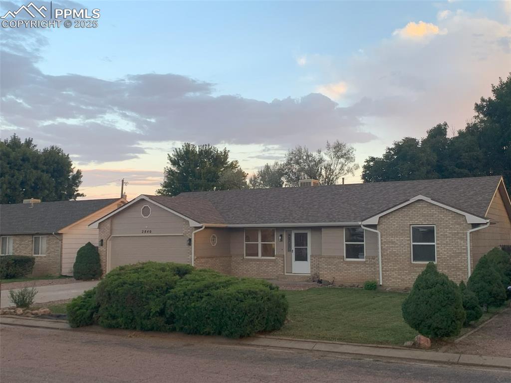 Caption: Single story home featuring roof with shingles, brick siding, a front lawn, and an attached garage
