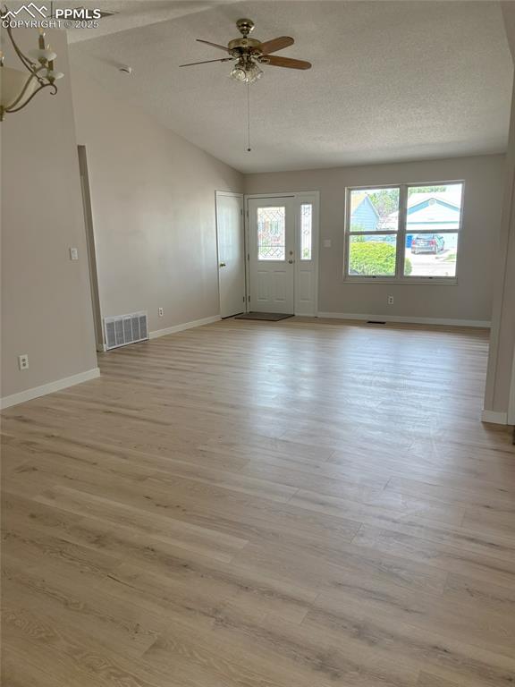 Image 2 of 6: Unfurnished living room featuring a textured ceiling, light wood-style floo