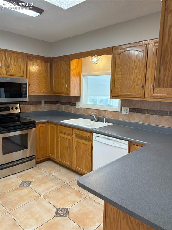 Image 4 of 6: Kitchen featuring stainless steel appliances, brown cabinetry, decorative b