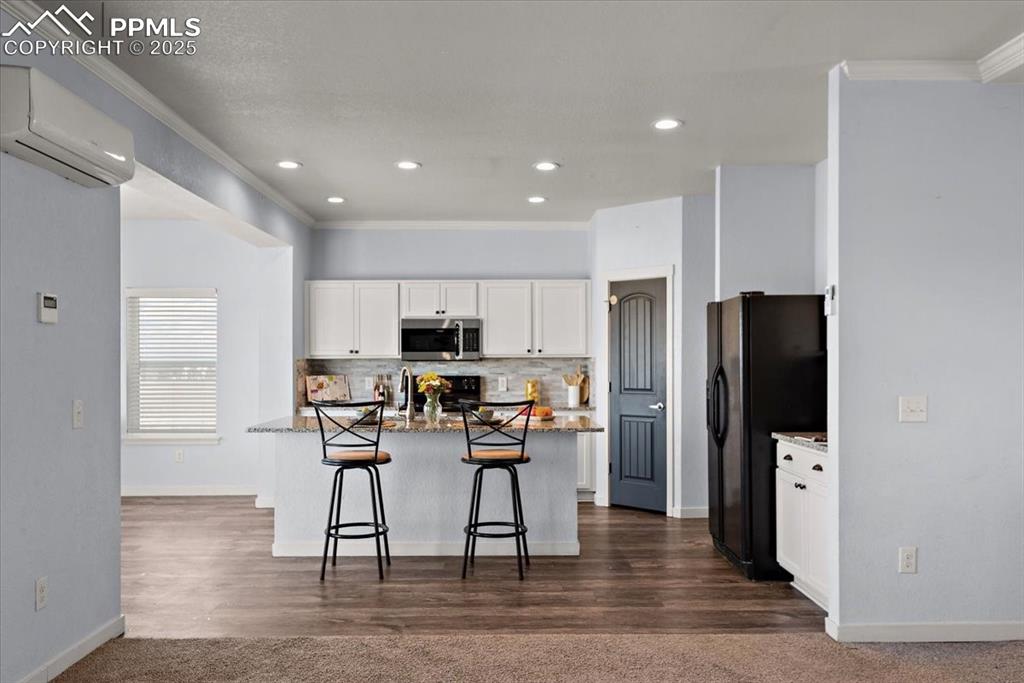 Image 13 of 33: Kitchen featuring stone counters, black appliances, a kitchen bar, white ca