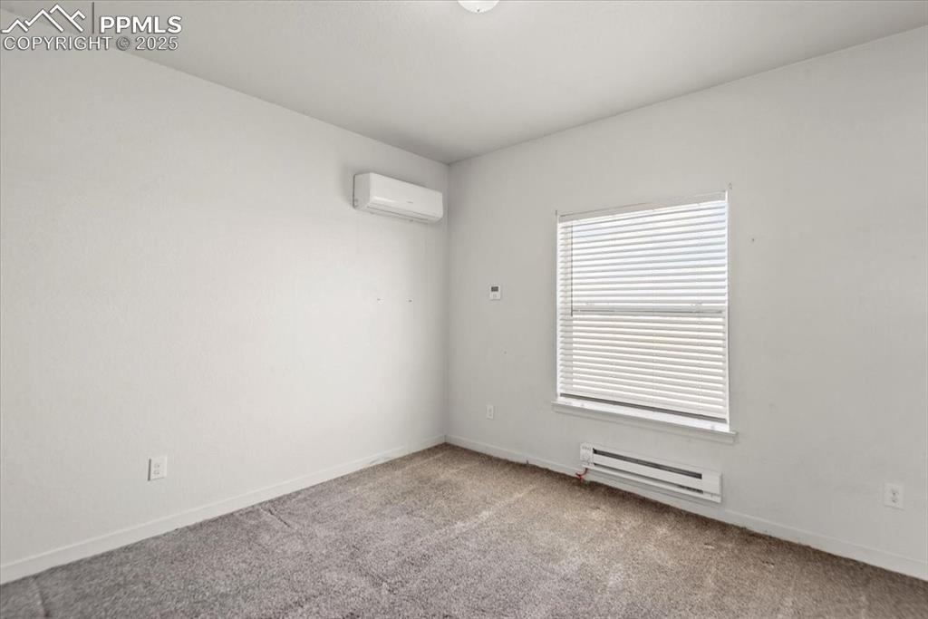 Image 21 of 33: Carpeted spare room with baseboard heating, a wall unit AC, and baseboards