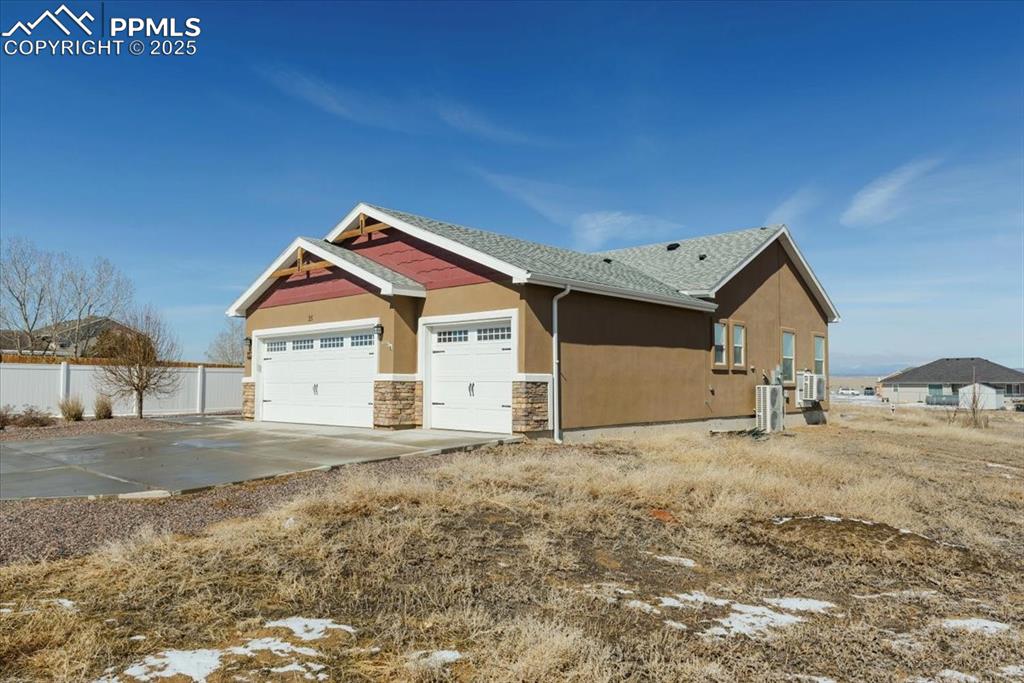 Image 4 of 33: View of side of home featuring a shingled roof, concrete driveway, stone si