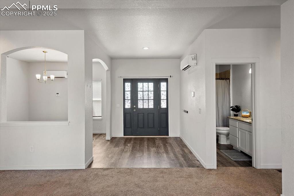 Image 6 of 33: Foyer featuring a chandelier, a wall unit AC, dark carpet, and a textured c
