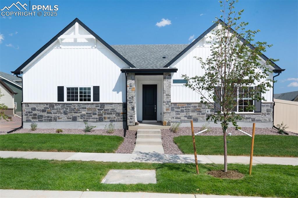Caption: View of front of house featuring board and batten siding, stone siding, a front yard, and roof with 