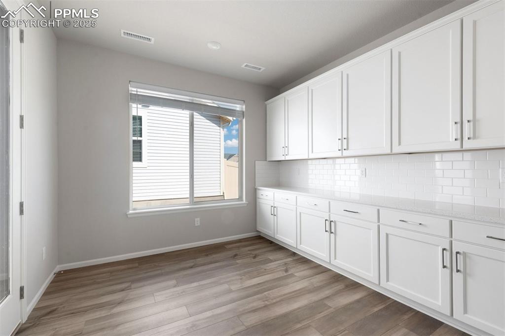Image 11 of 33: Kitchen featuring white cabinetry, light stone counters, light wood-type fl