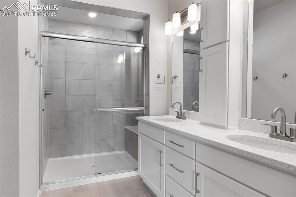 Image 25 of 33: Bathroom with a shower stall, double vanity, and light tile patterned floor
