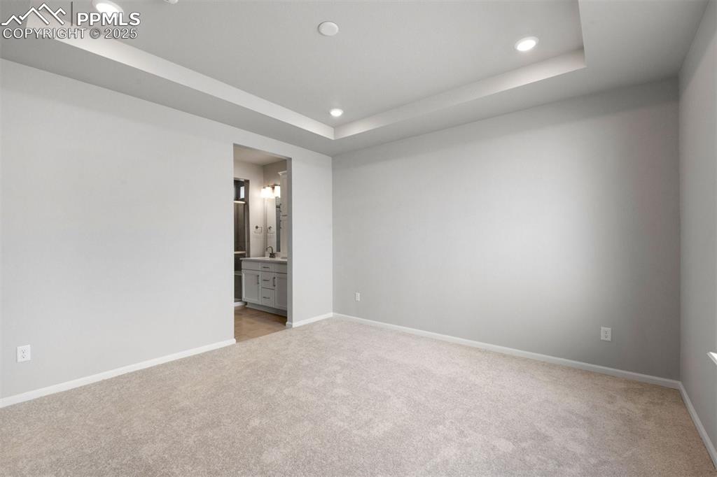 Image 26 of 33: Unfurnished bedroom with a tray ceiling, light colored carpet, ensuite bath