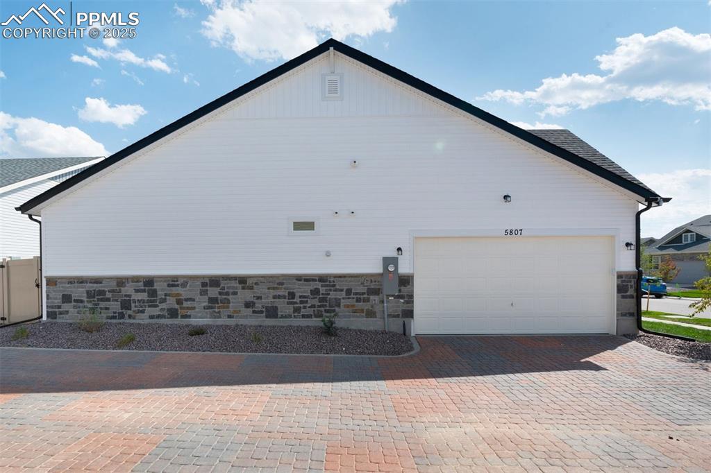 Image 5 of 33: View of side of property with stone siding, decorative driveway, and a gara