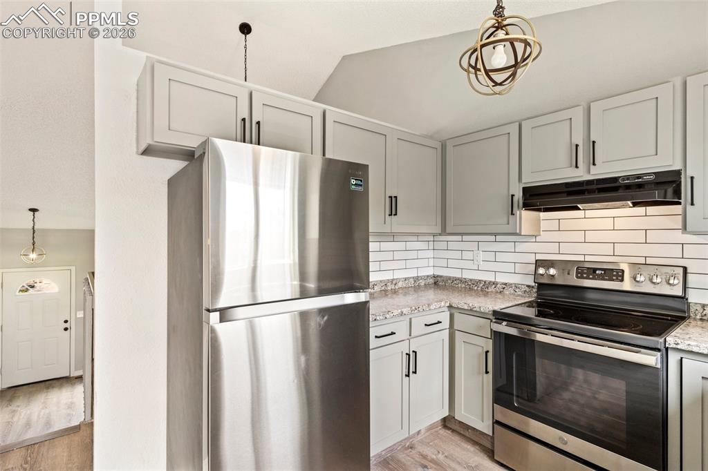 Image 12 of 35: Kitchen with pendant lighting, stainless steel appliances, backsplash, vaul