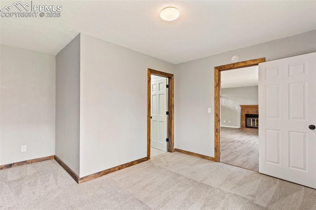 Image 26 of 35: Basement bedroom featuring light colored carpet and a brick fireplace