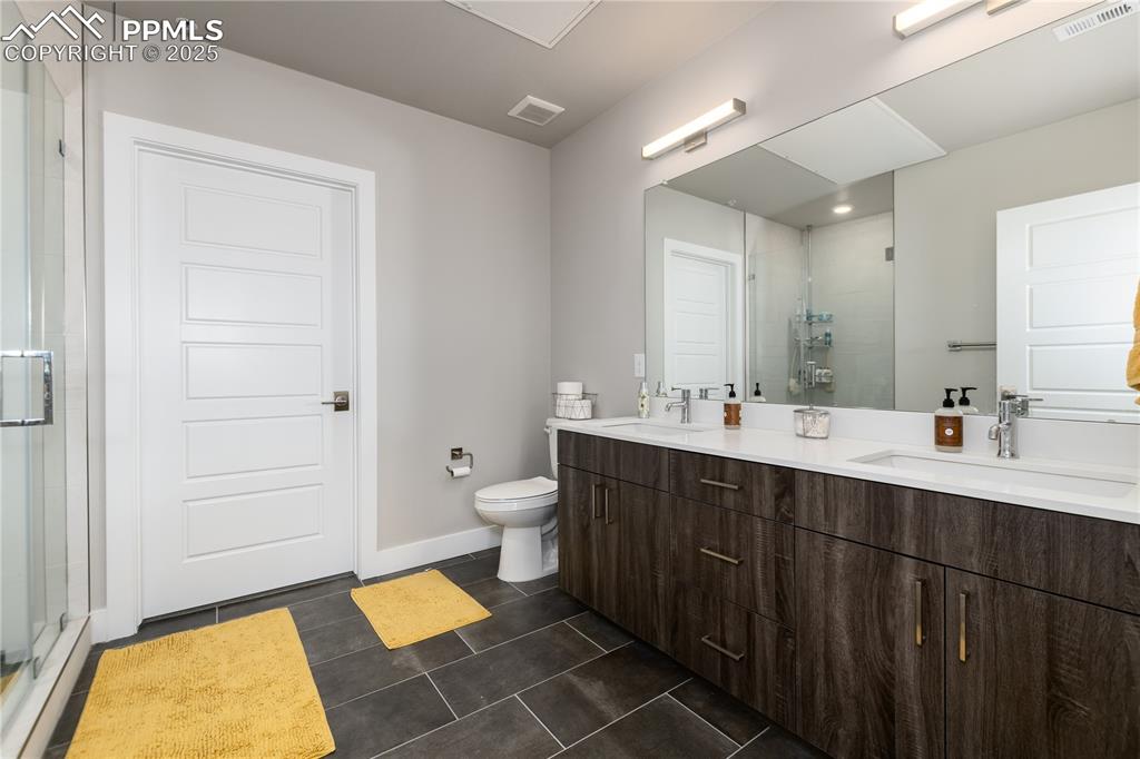 Image 17 of 21: Bathroom featuring double vanity, a stall shower, and dark tile patterned f
