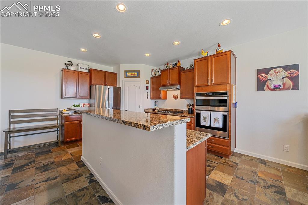 Image 10 of 35: Kitchen with stone tile floors, stainless steel appliances, stone counterto