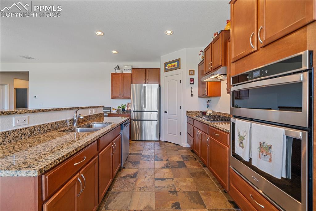 Image 11 of 35: Kitchen with stainless steel appliances, a sink, stone tile flooring, under