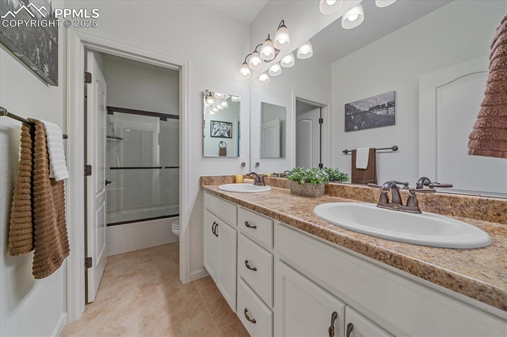 Image 21 of 35: Full bathroom with toilet, double vanity, enclosed tub / shower combo, and 