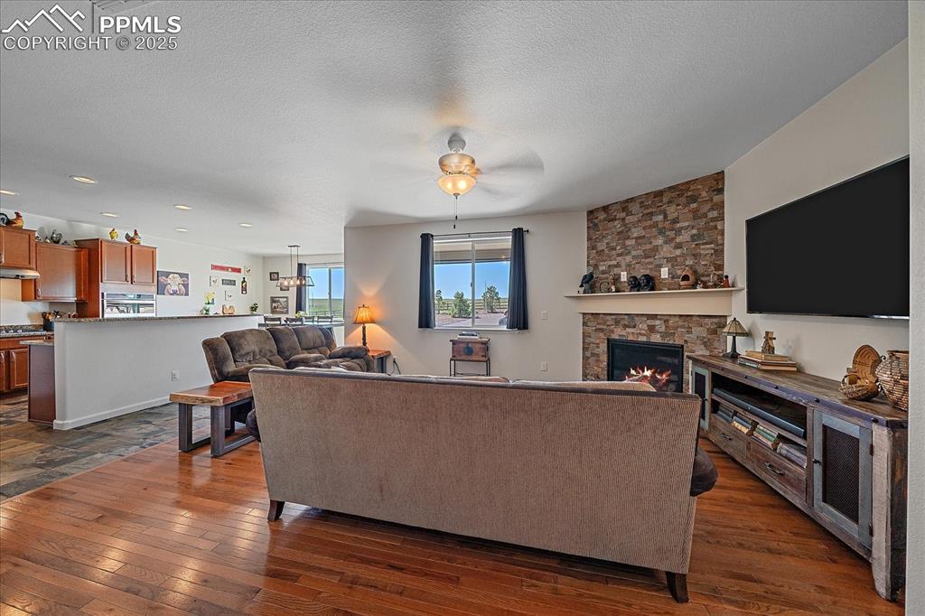 Image 6 of 35: Living area featuring dark wood-type flooring, a stone fireplace, a ceiling