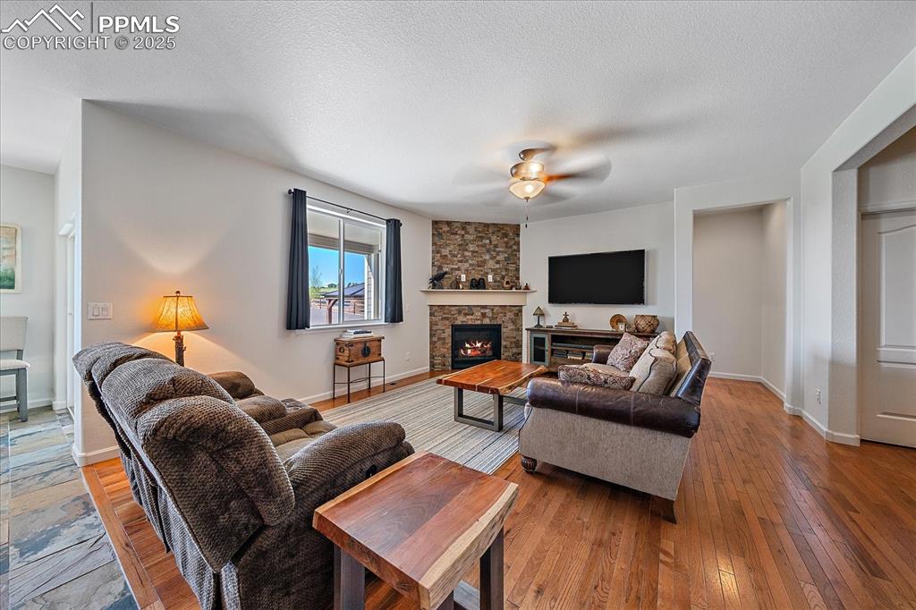 Image 7 of 35: Living area with a ceiling fan, a stone fireplace, light wood-style floorin