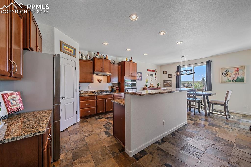 Image 9 of 35: Kitchen featuring stainless steel appliances, stone tile flooring, a center