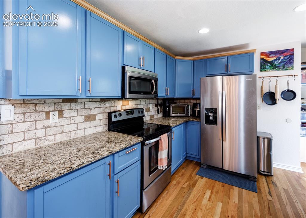 Image 12 of 47: Blue cabinetry with gold-tone hardware, granite countertops, brick-style ti