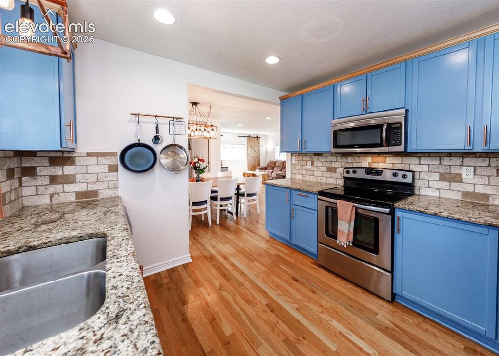 Image 15 of 47: Kitchen with wood-finish flooring, vibrant blue cabinetry, stainless steel