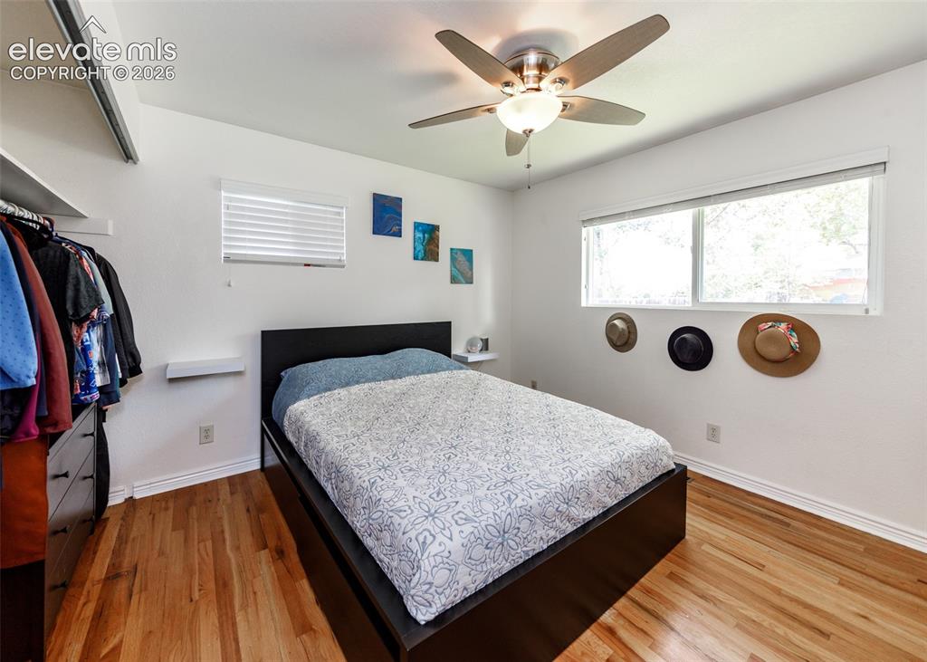 Image 18 of 47: Warm-toned wood flooring, ceiling fan with light fixture, and two windows p