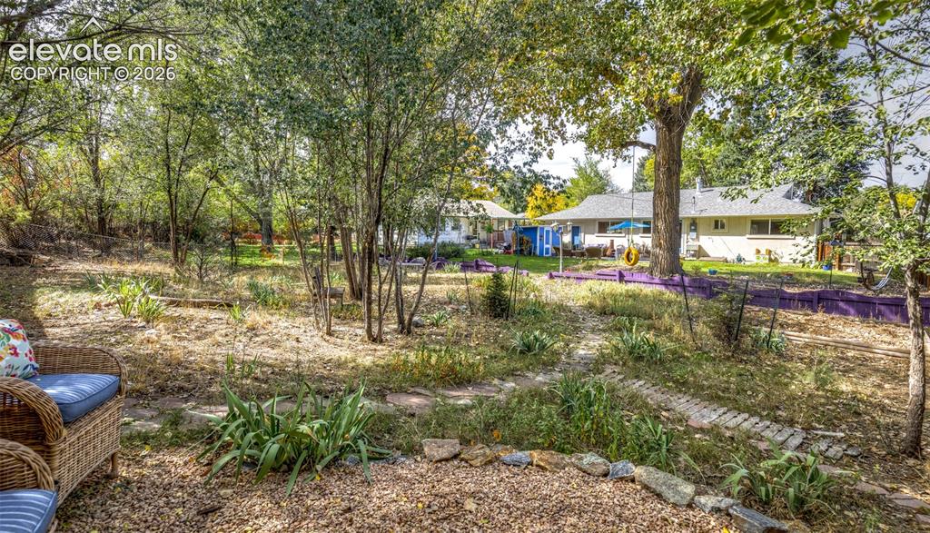 Image 36 of 47: Expansive backyard featuring mature trees, a gravel patio, and stone-edged