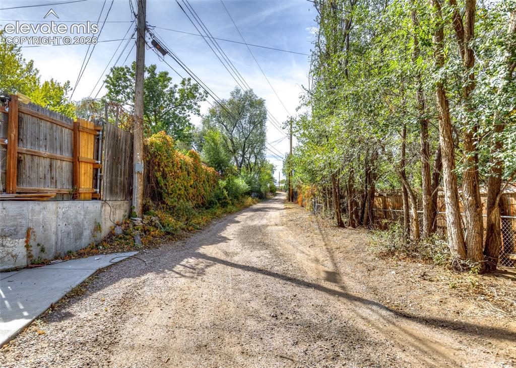 Image 38 of 47: Gravel pathway featuring a concrete sidewalk on one side and mature trees o