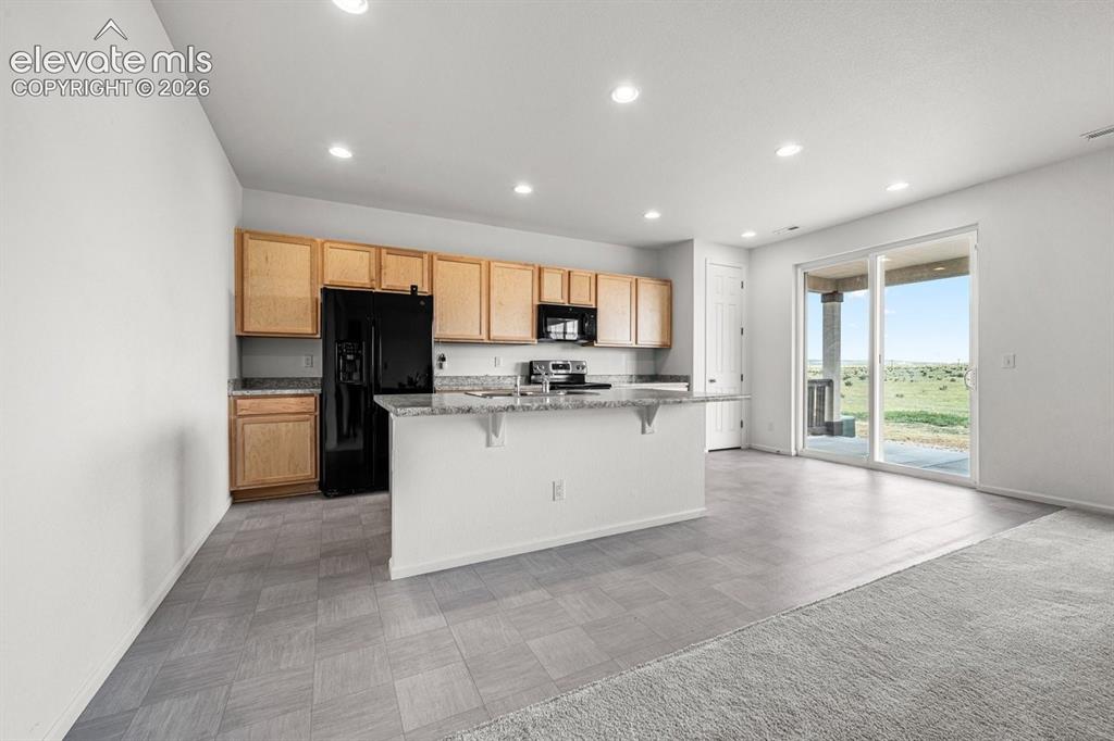 Image 10 of 25: Kitchen with wood cabinetry, black appliances, a central island with a gran