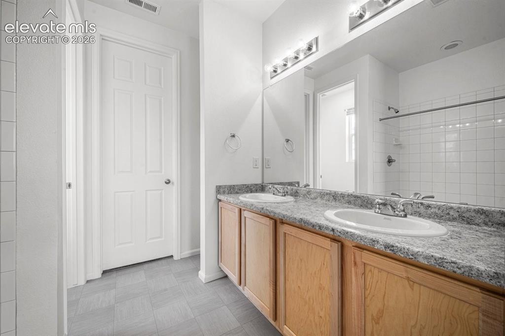 Image 15 of 25: Double vanity with laminate countertops, wood-finish cabinetry, and white p