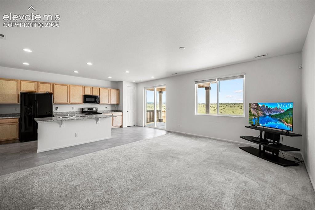 Image 17 of 25: Open-concept living space with light wood cabinetry, a kitchen island, and 