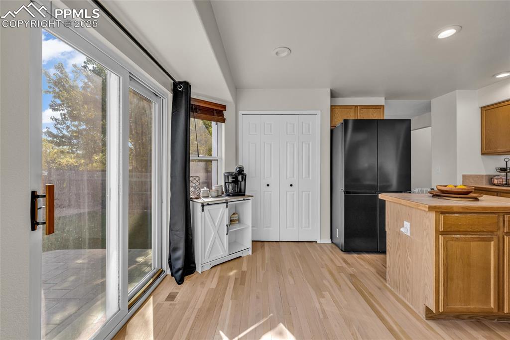 Image 10 of 40: Kitchen featuring freestanding refrigerator, brown cabinets, light wood-sty