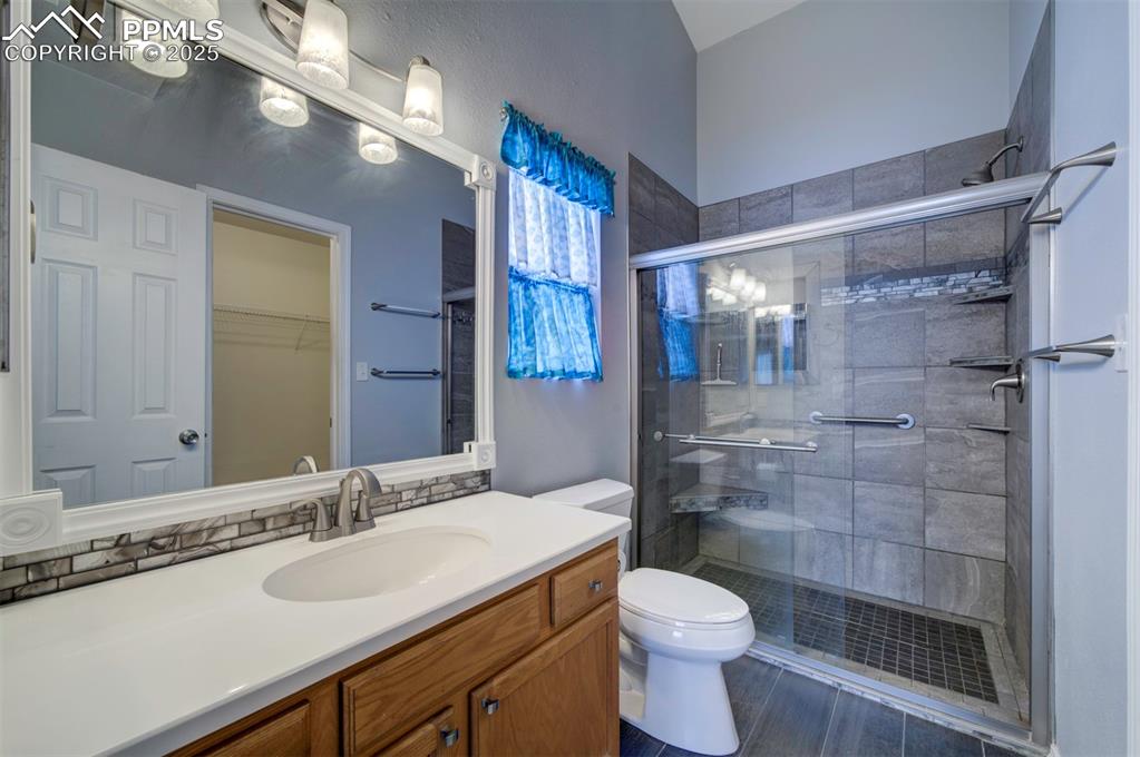 Image 19 of 30: Primary bathroom, tile shower, tile floor, walk in closet, vanity