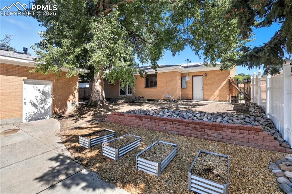 Image 21 of 30: Back of property featuring a vegetable garden, a patio, and brick siding