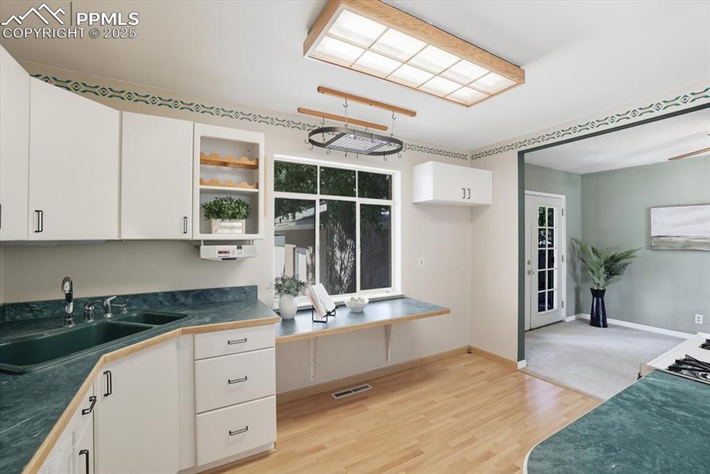Image 6 of 30: Kitchen featuring dark countertops, white cabinetry, light wood-style floor