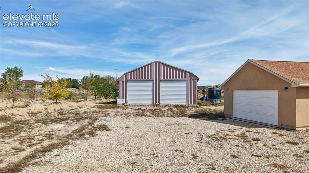 Image 10 of 50: Detached metal outbuilding featuring dual roll-up garage doors, accompanied