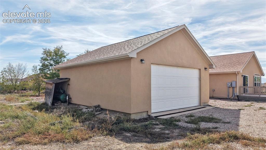 Image 11 of 50: Detached garage structure featuring a stucco exterior, shingled gable roof,