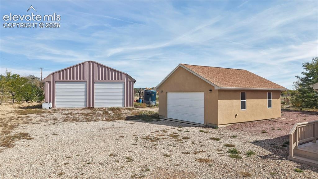Image 12 of 50: Detached structures including a metal two-bay garage and a single-bay stucc