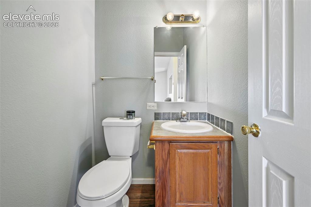 Image 15 of 50: Restroom featuring a wood-finish vanity with a stone countertop, integrated