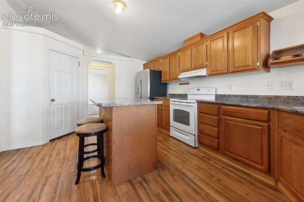 Image 21 of 50: Kitchen featuring wood cabinetry, an island with stone-surface countertop,