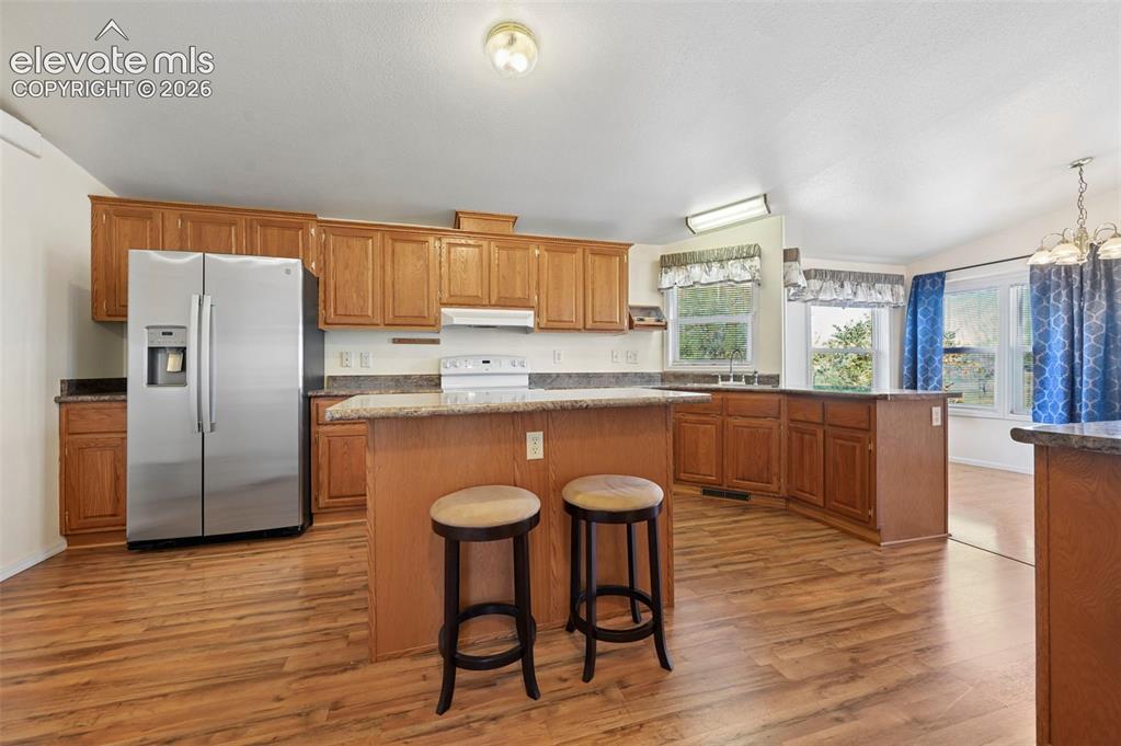 Image 22 of 50: Kitchen featuring wood-finish cabinetry, stone-surfaced countertops, a cent