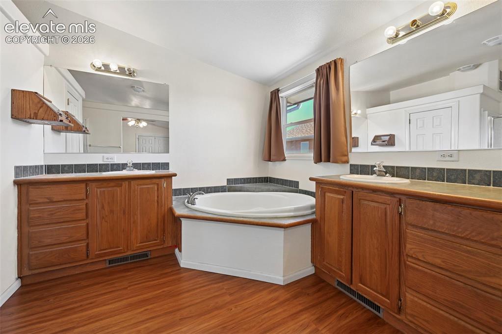 Image 42 of 50: Dual vanities with wood cabinetry, drop-in sinks, tiled backsplash, large w