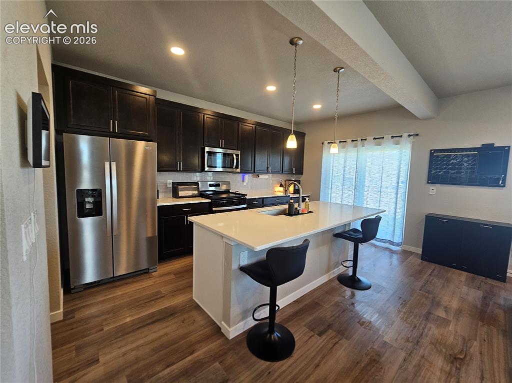 Image 16 of 35: Kitchen featuring wood-finish flooring, dark wood cabinetry, stainless stee