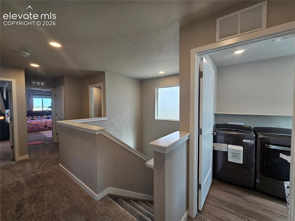 Image 18 of 35: Upper-level laundry closet with wood-finish flooring, recessed lighting, an