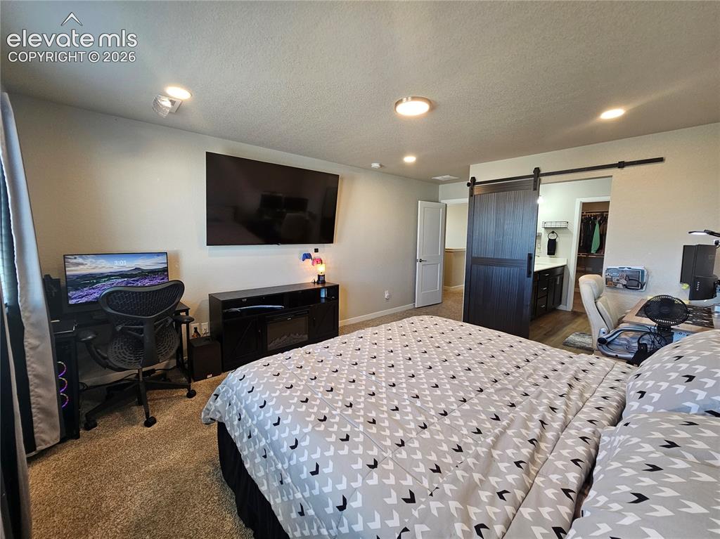 Image 27 of 35: Carpeted bedroom with recessed lighting and a dark wood-finish barn door