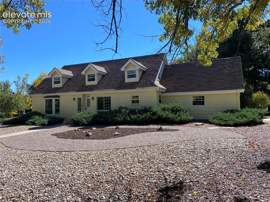 Caption: Two-story residence with dormer windows, light-toned siding, and a shingle roof
